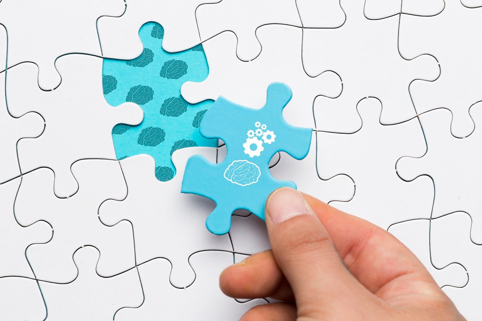close-up-of-human-hand-holding-blue-puzzle-piece-with-brain-and-cogwheel-drawing